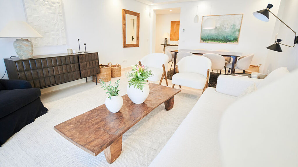Be Aloha – Marbella - lichte woonkamer met rustieke houten salontafel, witte fauteuils en bloemenvazen op crèmekleurig tapijt