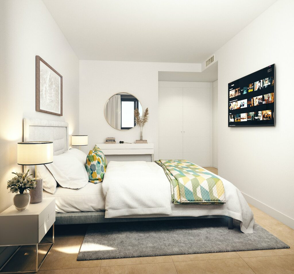 Habitat Alborán – Bora – Torremolinos – lyst moderne soveværelse med vægmonteret TV, geometrisk tæppe og rundt spejl over hvid vask