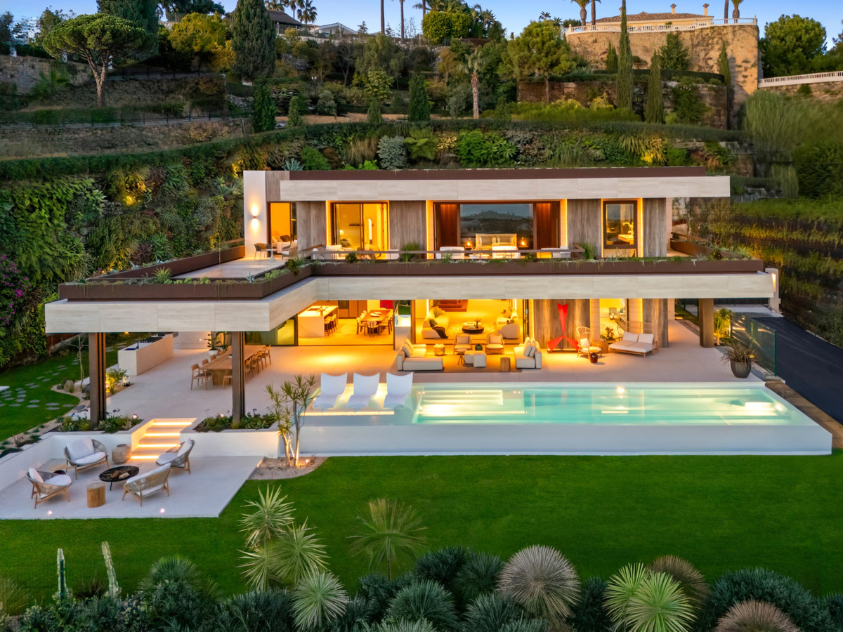 The Sky Marbella Villas – Benahavís – Luftaufnahme in der Abenddämmerung: moderne Luxusvilla mit beleuchteten Wohnbereichen, Infinity-Pool und Gartenanlage