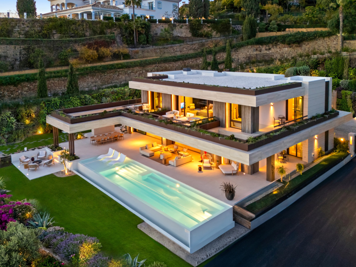 The Sky Marbella Villas – Benahavís – Luftaufnahme bei Dämmerung: moderne Luxusvilla mit offenen Wohnbereichen, großem Infinity-Pool und gepflegtem Garten