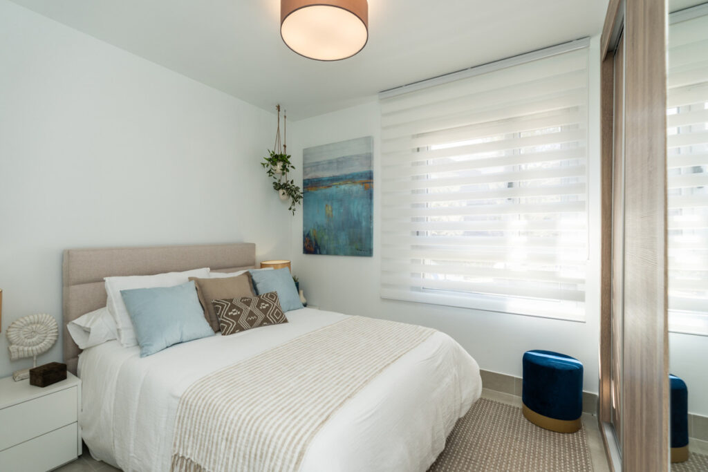 Solana Village – Fase 3 – La Cala Golf - elegantly styled bedroom with upholstered headboard, soft blue accents, and roller blinds