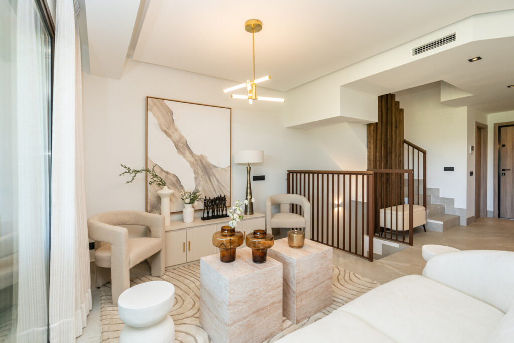 The Meadows – FASE 1 – La Cala Golf - elegant upper-level living room with cream boucle chairs, stone coffee tables, and wooden staircase balustrade