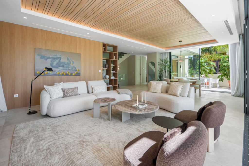 Belfry 1 – Estepona - offener Wohnbereich mit cremefarbenen Sofas, Holzwänden und nahtlosem Übergang zur Gartenterrasse